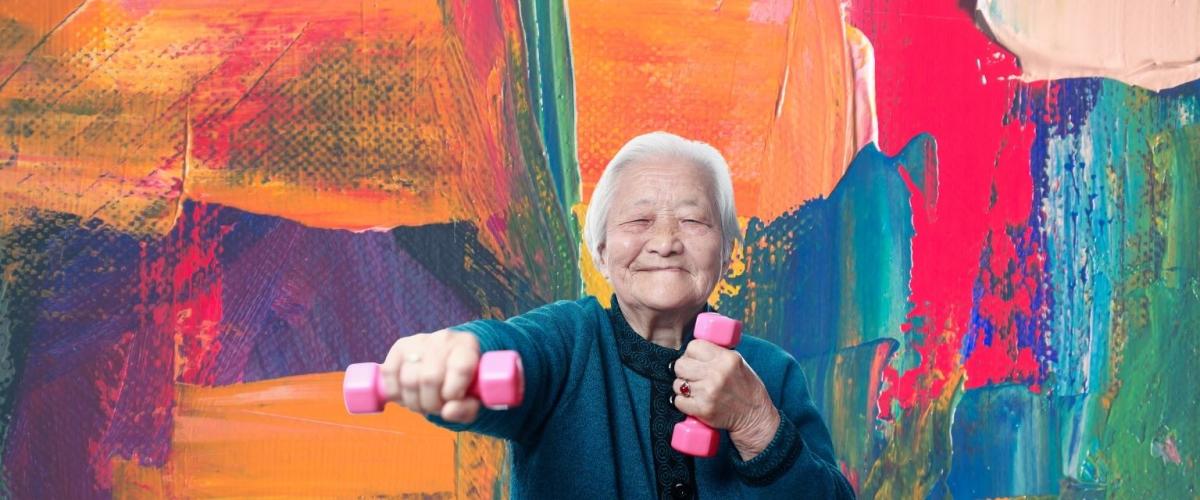 Older Asian woman smiling with pink handweights