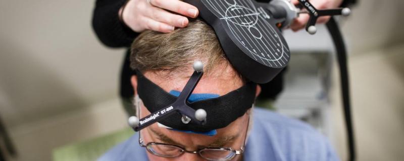 Man's head with magnetic stimulation device and technician's hands